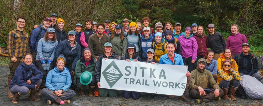 STW Volunteer group Edit_sm About 40 Sitka Trail Works volunteers, holding up a Sitka Trail Works sign.