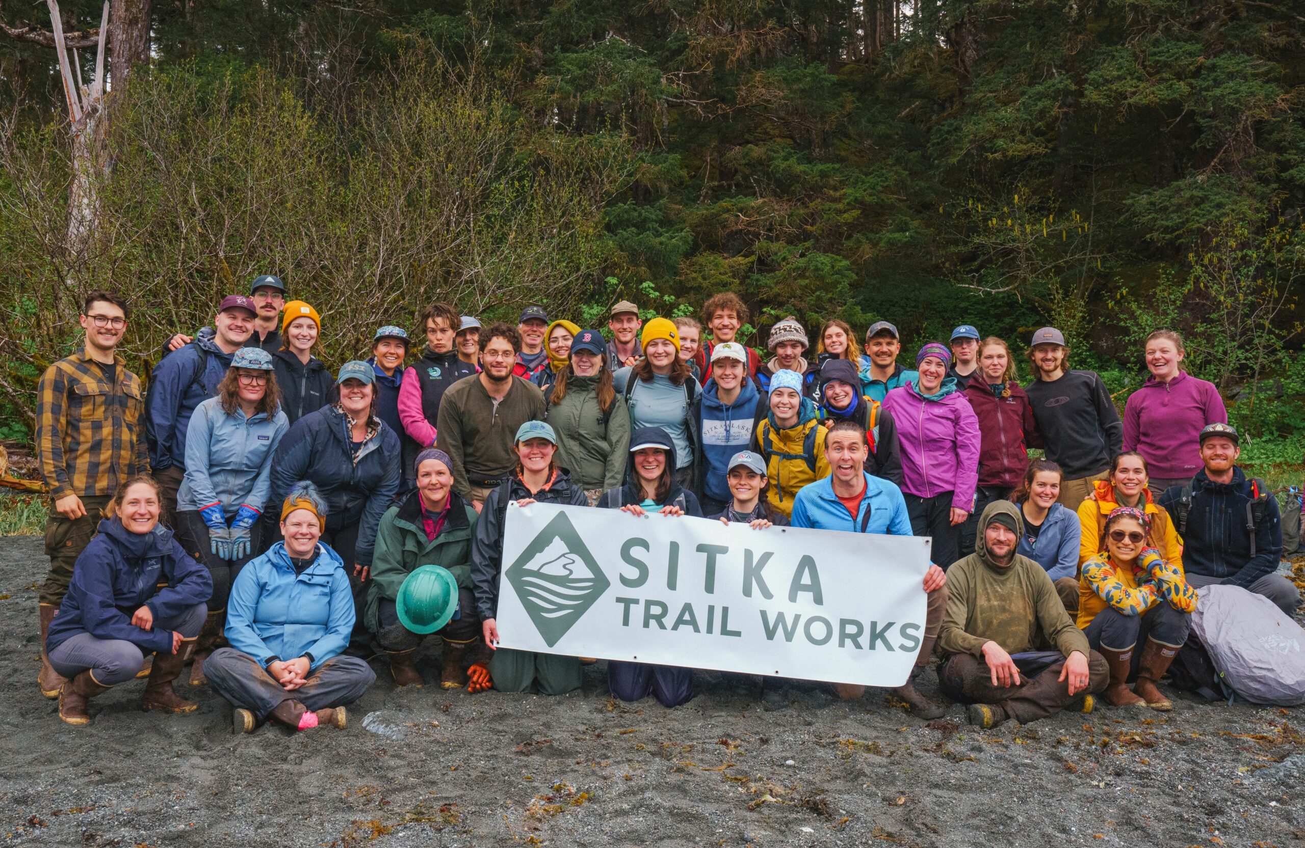 About 40 Sitka Trail Works volunteers, holding up a Sitka Trail Works sign.