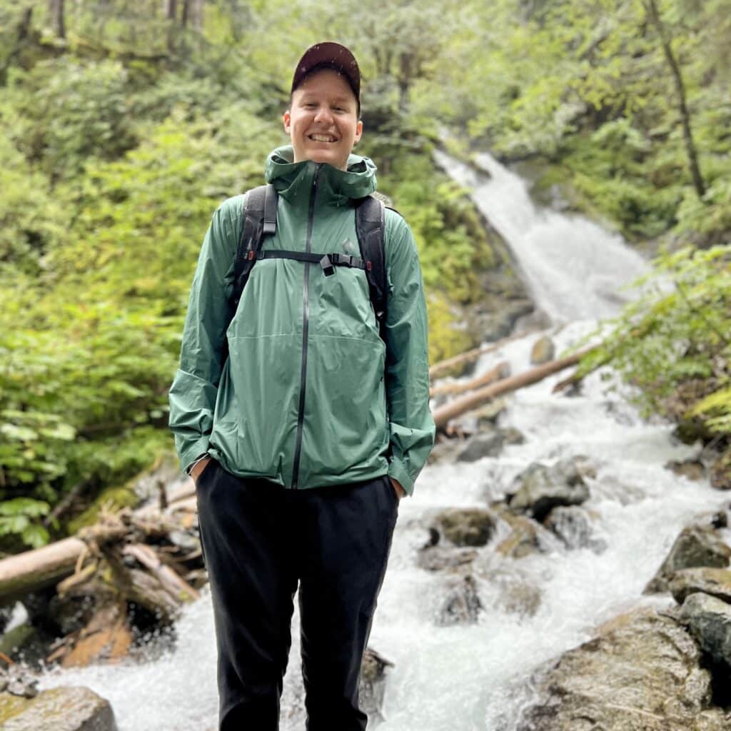 Photo of Colton Holmes standing in front of a waterfall